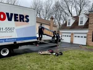 Workers from a AT Movers unloading furniture from a truck in front of a house.